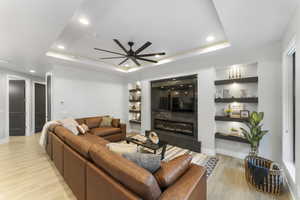 Living room featuring a tile fireplace, ceiling fan, a raised ceiling, and light hardwood / wood-style floors