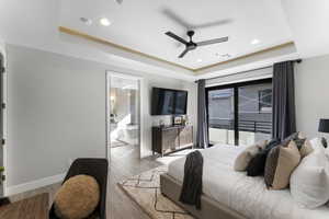 Bedroom featuring ceiling fan, hardwood / wood-style flooring, a tray ceiling, ensuite bath, and access to exterior