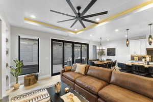 Living room featuring ceiling fan with notable chandelier, light hardwood / wood-style floors, and a tray ceiling