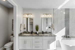 Bathroom with a bath, toilet, double sink vanity, and tile walls