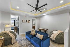 Living room featuring wood-type flooring, ceiling fan, and a raised ceiling