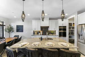 Kitchen with tasteful backsplash, stainless steel appliances, a breakfast bar area, light stone countertops, and a kitchen island with sink