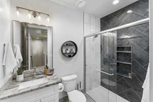 Bathroom featuring a shower with door, toilet, and vanity