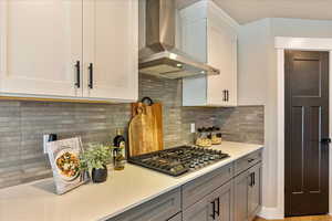 Kitchen with white cabinetry, wall chimney exhaust hood, stainless steel gas cooktop, tasteful backsplash, and gray cabinets