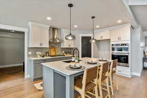 Kitchen featuring pendant lighting, white cabinetry, wall chimney range hood, and stainless steel appliances