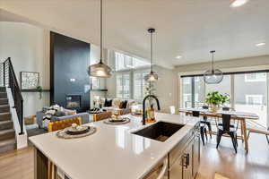 Kitchen with sink, pendant lighting, a fireplace, a center island with sink, and light wood-type flooring