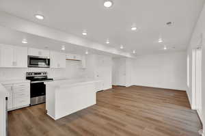 Kitchen featuring appliances with stainless steel finishes, white cabinetry, wood-type flooring, and a kitchen island