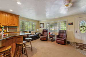 Interior space with dark stone countertops, crown molding, tasteful backsplash, light carpet, and a kitchen bar