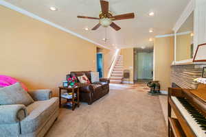 Carpeted living room with a fireplace, crown molding, and ceiling fan