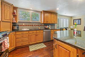 Kitchen with a textured ceiling, dark hardwood / wood-style flooring, stainless steel appliances, decorative backsplash, and sink