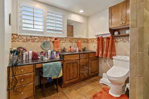 Bathroom featuring vanity, tile patterned floors, tile walls, toilet, and backsplash