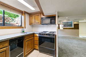 Kitchen featuring black appliances, sink, light stone counters, a textured ceiling, and light tile patterned floors