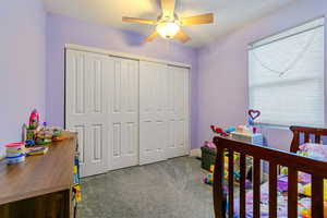 Carpeted bedroom with ceiling fan and a closet