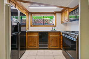 Kitchen featuring sink, black appliances, a textured ceiling, and light tile patterned floors