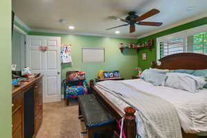 Carpeted bedroom with ceiling fan and ornamental molding