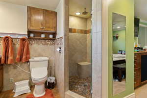 Bathroom featuring tile walls, tile patterned floors, toilet, and a tile shower