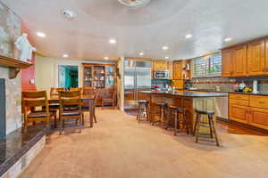 Kitchen with stainless steel appliances, light carpet, a center island, a breakfast bar area, and a textured ceiling