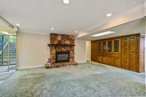 Unfurnished living room with ornamental molding, carpet, a textured ceiling, and a stone fireplace