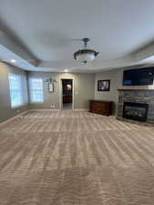 Master bedroom featuring carpet floors, a stone fireplace, and a raised ceiling