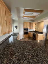 Kitchen featuring tile patterned floors, stainless steel appliances, sink, dark stone countertops, and kitchen peninsula