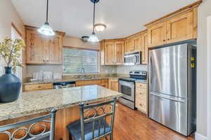 Kitchen with stainless steel appliances, hardwood / wood-style floors, sink, decorative light fixtures, and light stone countertops