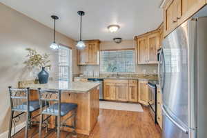 Kitchen featuring a breakfast bar area, light wood-type flooring, stainless steel appliances, pendant lighting, and sink