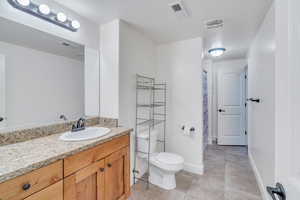 Bathroom featuring vanity, tile patterned floors, a textured ceiling, and toilet