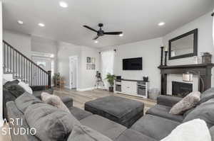 Living room with a tile fireplace, light wood-type flooring, and ceiling fan