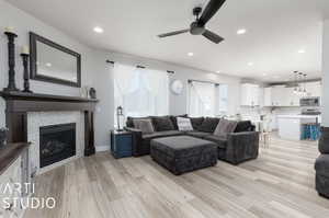 Living room featuring sink, a tiled fireplace, light wood-type flooring, and ceiling fan