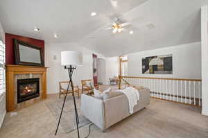 Carpeted living room with a tiled fireplace, ceiling fan, and lofted ceiling