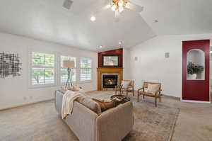 Carpeted living room featuring a tile fireplace, ceiling fan, and vaulted ceiling