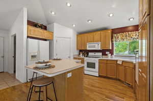 Kitchen with light wood-type flooring, white appliances, a kitchen island, a breakfast bar, and lofted ceiling