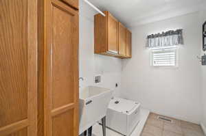 Laundry area featuring light tile patterned flooring, hookup for an electric dryer, washer hookup, cabinets, and sink