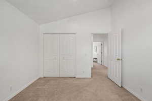 Unfurnished bedroom with vaulted ceiling, light colored carpet, and a closet