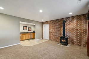 Unfurnished living room featuring light colored carpet, brick wall, and a wood stove