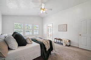 Bedroom featuring lofted ceiling, a textured ceiling, carpet, and ceiling fan