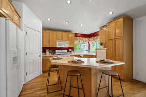 Kitchen with light hardwood / wood-style flooring, a center island, a kitchen breakfast bar, and white appliances