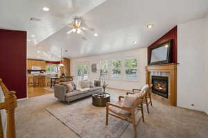 Living room featuring a fireplace, light carpet, ceiling fan, and lofted ceiling