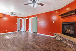 Unfurnished living room featuring ceiling fan, dark hardwood / wood-style floors, a fireplace, and a textured ceiling