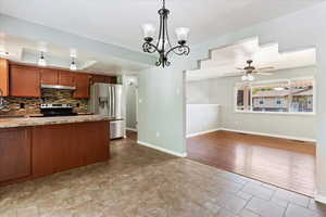 Kitchen featuring stainless steel appliances, hanging light fixtures, ceiling fan with notable chandelier, decorative backsplash, and light hardwood / wood-style flooring