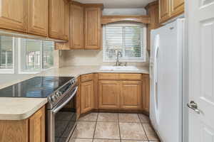 Kitchen with white fridge with ice dispenser, stainless steel range with electric cooktop, sink, light tile patterned floors, and backsplash