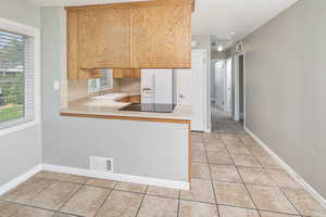 Kitchen with tasteful backsplash, sink, kitchen peninsula, white refrigerator with ice dispenser, and light tile patterned flooring