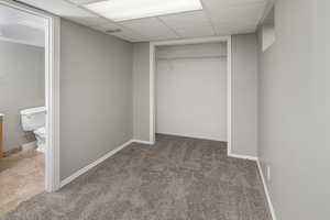 Unfurnished bedroom featuring a paneled ceiling, carpet, a closet, and connected bathroom