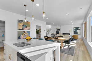 Kitchen featuring sink, hanging light fixtures, light hardwood / wood-style floors, a kitchen island with sink, and white cabinetry