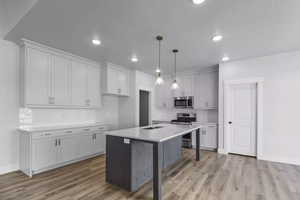 Kitchen featuring appliances with stainless steel finishes, hanging light fixtures, light hardwood / wood-style floors, a kitchen island, and decorative backsplash