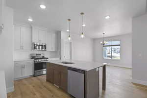 Kitchen featuring stainless steel appliances, an inviting chandelier, hanging light fixtures, light hardwood / wood-style floors, and a kitchen island with sink