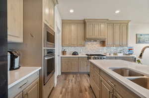 Kitchen with tasteful backsplash, hardwood / wood-style floors, light brown cabinets, sink, and appliances with stainless steel finishes