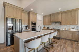 Kitchen with stainless steel appliances, wood-type flooring, tasteful backsplash, and a center island with sink