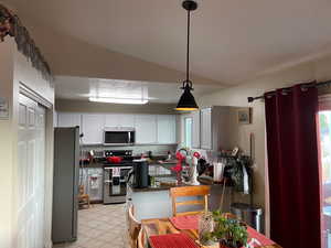 Kitchen with light tile patterned flooring, stainless steel appliances, white cabinetry, backsplash, and vaulted ceiling