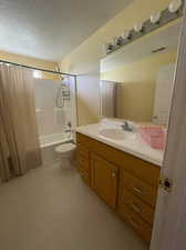 Full bathroom featuring vanity, shower / bathtub combination with curtain, a textured ceiling, and toilet